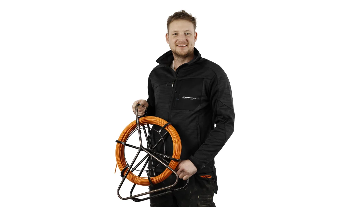 Monteur houdt een trekveer en een haspel vast om kabel door een bestaande leiding te trekken