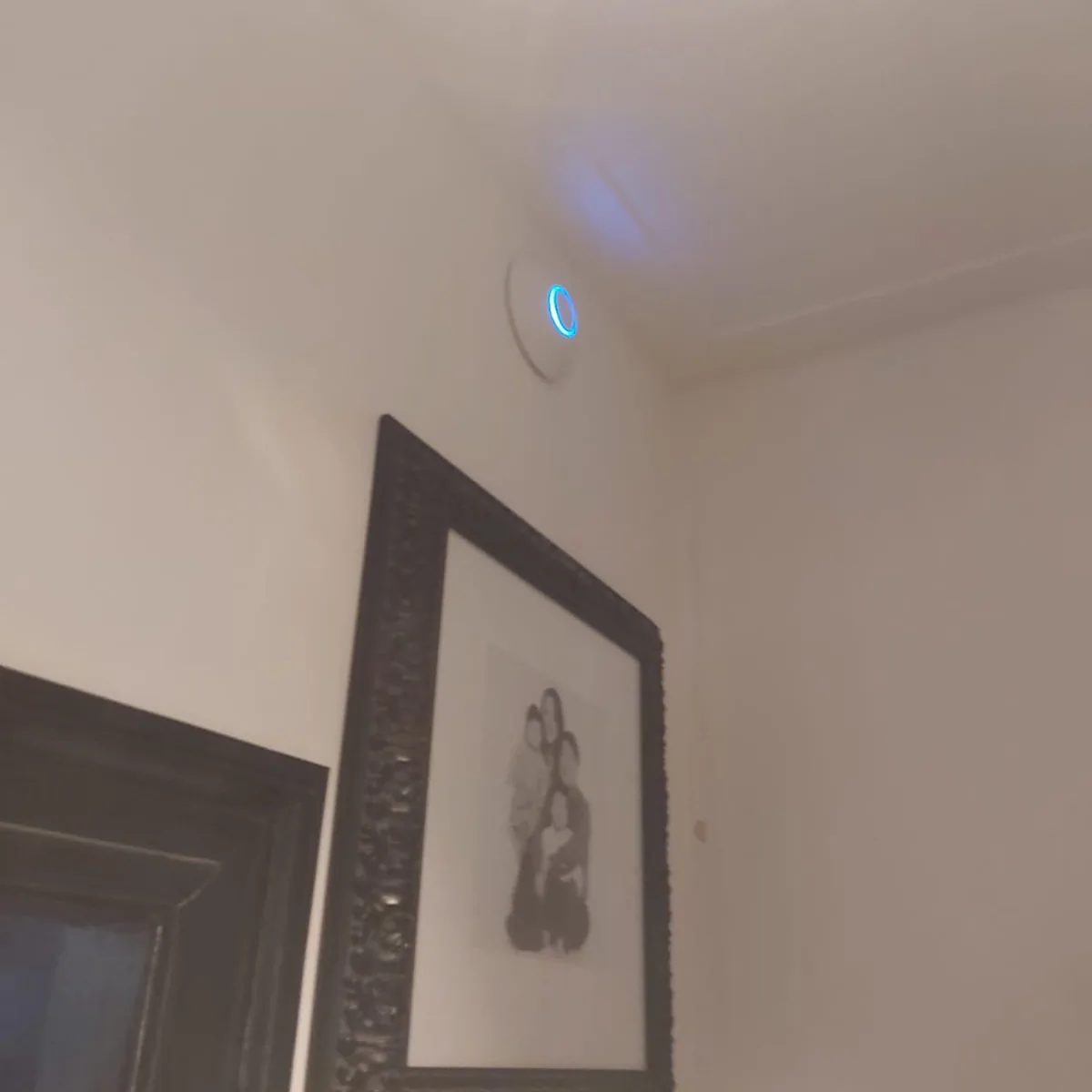 Wifi-punt vlak bij het plafond in een gang, naast een ingelijste tekening
